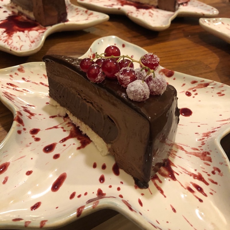 Slice of chocolate mousse cake topped with sugared red currants on a star-shaped plate splashed with berry sauce