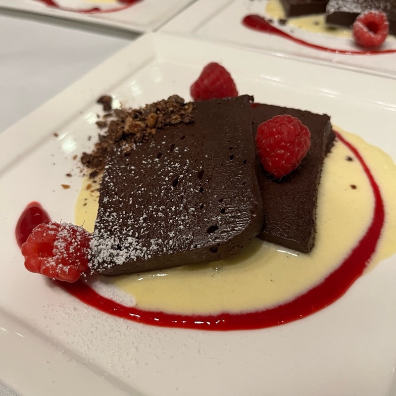 Chocolate terrine dusted with powdered sugar on crème anglaise with raspberry sauce and fresh raspberries