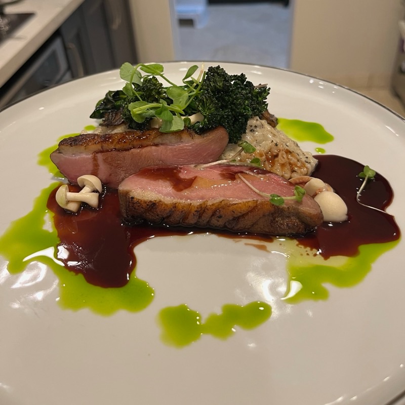 Sliced seared duck breast with dark jus, green herb oil, crispy kale and beech mushrooms