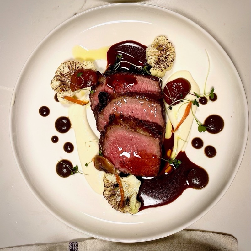 Sliced medium-rare ribeye with roasted cauliflower, a white purée and dots of dark pan sauce