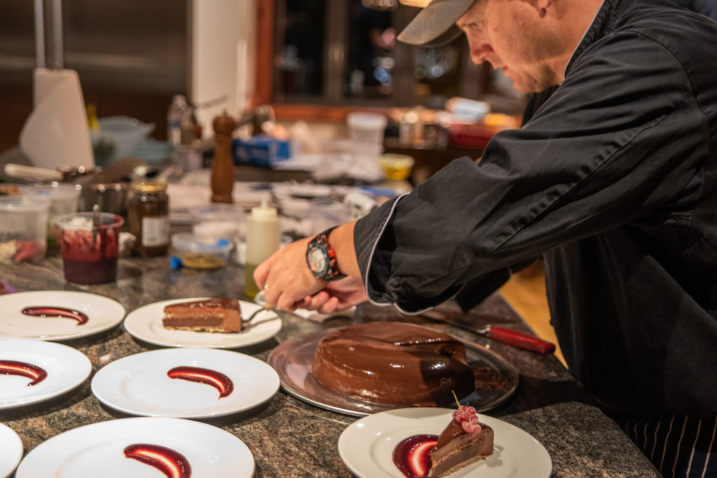 Chef Colin plating slices of chocolate cake with raspberry sauce at a villa kitchen counter