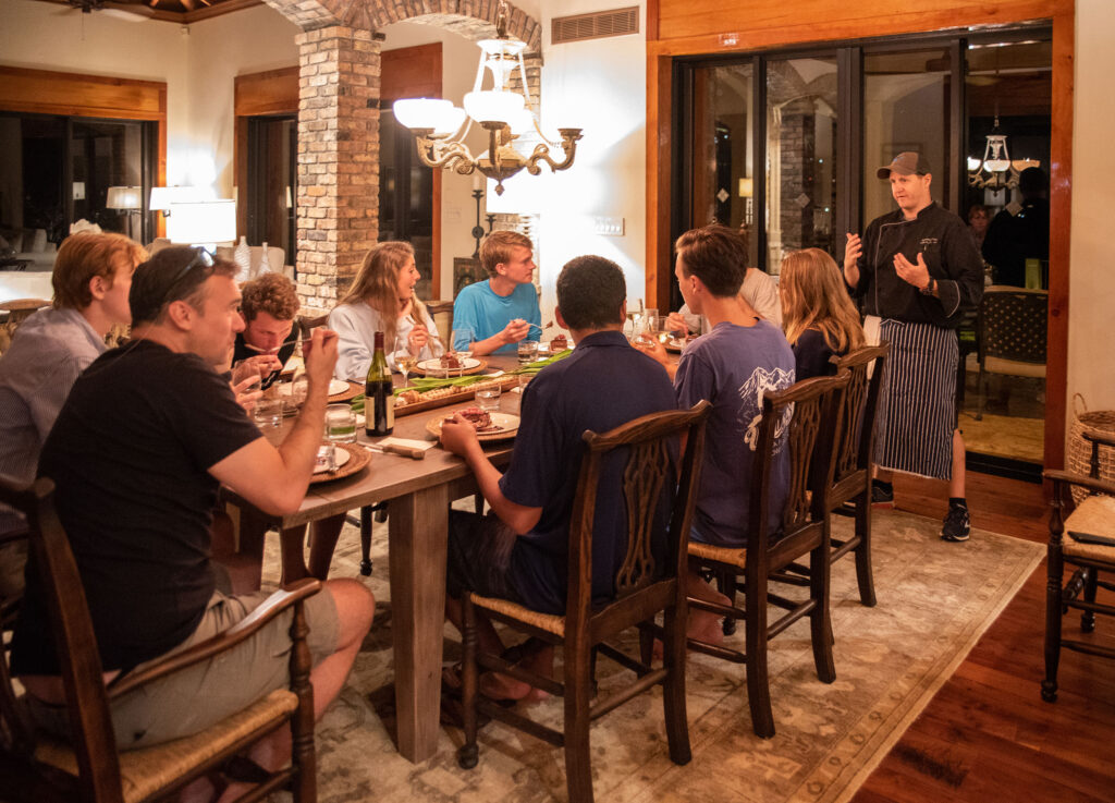 Chef Colin Auchincloss introducing the next course to a long table of guests at a villa dinner
